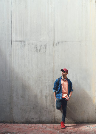 Young man, student and relax against wall, headphones and music on university campus with future and...