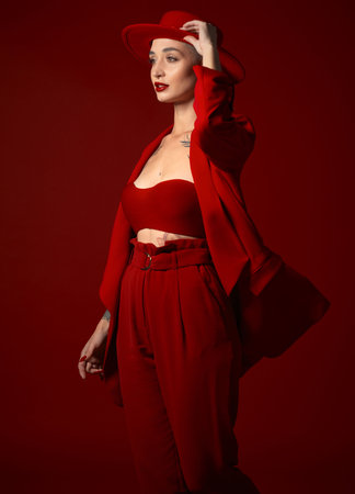 Vision, fashion and a woman in a hat on a red background in studio for elegant or trendy style. Aesthetic, beauty and future with a confident young female person looking edgy or classy in a bold suitの写真素材