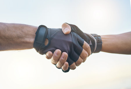 Teamwork, cycling and sports men shaking hands outdoor together against a sky background with flare. Handshake, fitness and partnership with a cyclist team saying thank you during a cardio workoutの写真素材