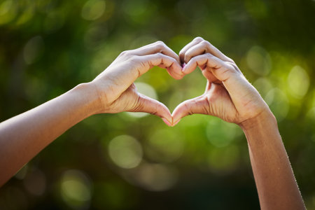 Hands, heart as a symbol or love or health with a person outdoor in nature on a blurred background for sustainability. Like, romance or valentines day with green gesture in a garden or yard in summerの写真素材