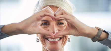 Portrait, hands and heart with a business woman in the office, feeling love for her corporate career. Face, emoji or hand sign with a senior female manager or ceo work looking happy and confidentの写真素材