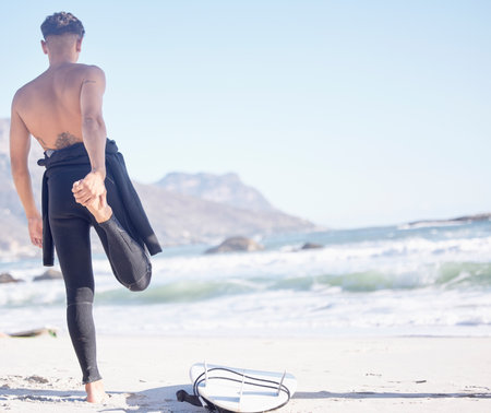 Back, man and stretching for beach surfing with waves, freedom and summer blue sky mockup in Cape Town. Surfer guy warm up legs at sea, sunshine and travel for water sports, adventure or ocean natureの写真素材
