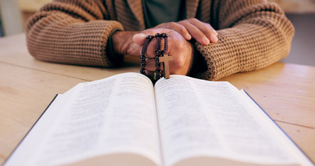 Hands, rosary and bible with closeup for faith, peace and hope at desk, home or praying for worship. Person, cross and jewelry for religion, mindfulness and connection to holy spirit, Jesus or Godの写真素材