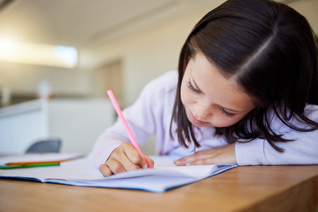 Little schoolgirl doing homework at table. Smart elementary aged child writing in notebookの写真素材