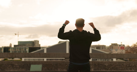 Man, runner or cheers in city for exercise time, fitness progress or training goal. Male person, athlete or victory or workout performance or cloudy morning in street, challenge or health celebrationの写真素材