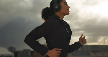 Fitness, music and a woman running in the city for health or cardio preparation of a marathon. Exercise, wellness or sports training and a young runner or athlete listening to audio with headphonesの写真素材