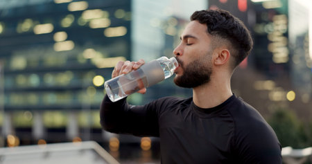 Man, drinking water and fitness in city after workout, exercise or outdoor training for natural sustainability. Thirsty male person with mineral drink in rest, recovery or break for hydration in townの写真素材