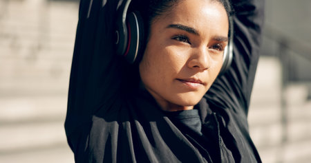 Fitness, headphones and woman stretching in city, workout and exercise for body health. Music, athlete and serious person warm up arms in urban town, listen to radio sound on technology and thinkingの写真素材