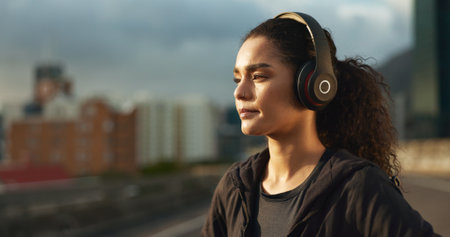 Woman, runner and headphones in city for fitness in evening sunset, music playlist workout sports. Female person, listen track and training thinking on street for cardio audio, exercise or streamingの写真素材