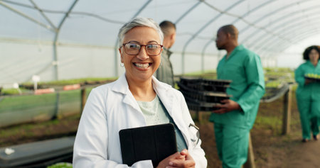 Portrait, botanist and happy woman at greenhouse with tablet tech for science at farm, plant and ecology. Face, smile and mature scientist at nursery for agriculture in glasses for research in Mexicoの写真素材