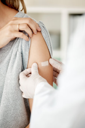vaccine and injection with a doctor placing a plaster on the arm of a female patient in the hospital...