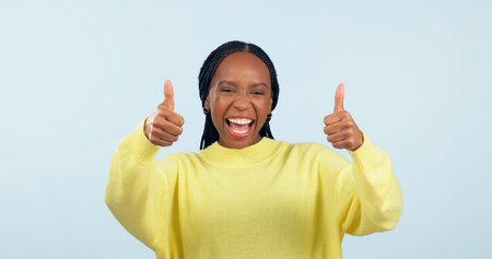 Portrait, smile and black woman with thumbs up, support and decision on a blue studio background. Face, African person and model with hand gesture, opportunity and feedback with review and emojiの写真素材