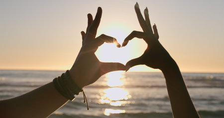 Love, hands and heart on beach with sunset, water background and horizon for vacation, travel or...