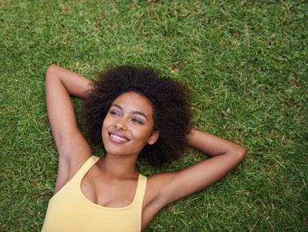 Planning the rest of her lazy day. a happy young woman lying on the grass.
