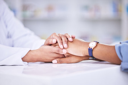Woman, pharmacist and holding hands for healthcare, support or trust on counter at the pharmacy. Closeup of female person or medical professional with patient in care for consultation, help or adviceの写真素材