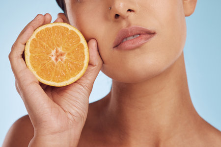 Woman, hands and orange for vitamin C, skincare or diet against a blue studio background. Closeup of female person holding organic citrus fruit for natural nutrition, dermatology or healthy wellnessの写真素材