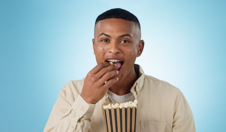 Portrait, happy man and popcorn for cinema in studio on blue background for entertainment mockup....