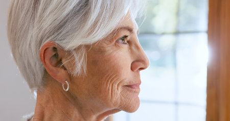 Senior, woman and face with thinking by window of memory, alzheimer and idea in retirement home with smile. Elderly, person and thoughtful with nostalgia, remember and relax in assisted livingの写真素材