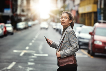 Phone, portrait of woman and cross street for journey, sunset commute and social media on internet. Mobile, consultant and person walk in city on smartphone for business, cbd travel and lens flareの写真素材