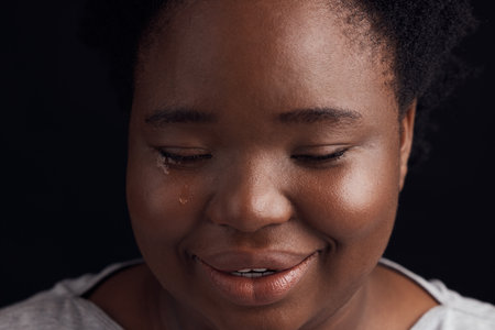 Crying, sad and a black woman on a studio background with depression, fear or mental health. Studio, face and an African girl or person with tears, frustrated or fail from a mistake on a backdropの写真素材