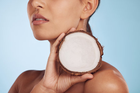Woman, coconut fruit and beauty, skincare or vegan cream isolated studio, blue background. Model or person hands with natural product for dermatology, eco friendly cosmetics and oil benefitsの写真素材