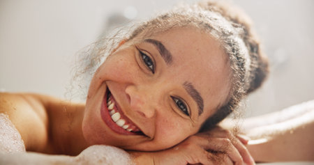 Health, smile and face of a woman in the bath at her home for zen, calm or self care routine. Happy, peace and headshot portrait of young female person relaxing in a tub in the bathroom in apartment.の写真素材