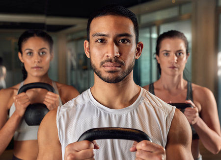 Were here for fitness. Cropped portrait of three young athletes working out with kettle bells in the gym.の写真素材