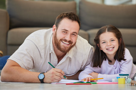 Father and daughter doing homework together drawing pictures and having fun. Dad teaching daughter while using book and colouring pencilsの写真素材