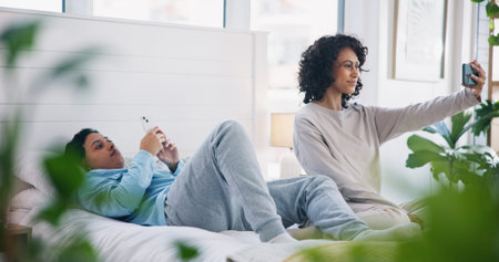 Smile, phone and lesbian couple on bed in selfie, love and relax together in eco friendly apartment....