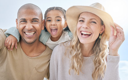 Summer, blue sky and portrait of young family having fun, laugh and play together. Multicultural mom, dad and girl outdoors on beach holiday and vacation. Love, bonding and couple with kid on weekendの写真素材