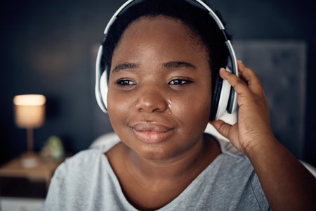 Crying, sad and black woman with headphones for music, sound or audio. Tears, radio and plus size African person listening, hearing and streaming podcast with depression, crisis and problem in homeの写真素材