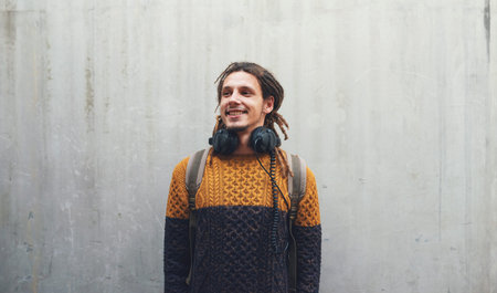 Student, fashion and gen z male with music headphones outdoors, happy and in stylish clothes on wall...