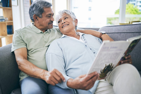 Couple, relax and reading book together on sofa in living room with love, care and quality time. Senior man, happy woman and married partner enjoy discussion with books on couch at home in retirementの写真素材