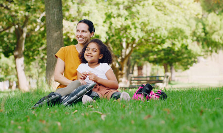 Family, mother and kid in park with rollerblading outdoor, relax on grass and fun in nature with happy people. Woman, girl and taking a break, sports and quality time together with love and careの写真素材