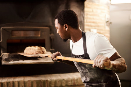 Support your local baker. a male baker removing freshly baked bread from the oven.の写真素材