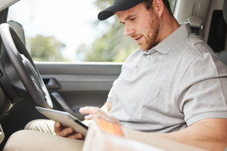 Whats the address again. a handsome young delivery man using a tablet while sitting in his van.