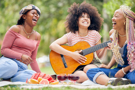 Friends, picnic in nature with guitar and smile or laugh as woman play music instrument. Black woman...