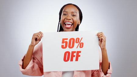 Portrait, sale sign or happy black woman by discount deal, 50 percent off offer or launch ad. Excited, smile or person with board for message, marketing or promotion card on grey background in studioの写真素材