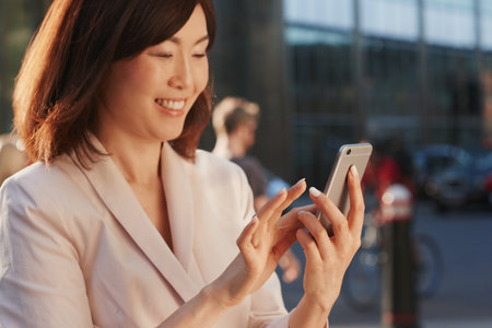 Connect with the world wherever you are. a young businesswoman using a smartphone against an urban background.の写真素材
