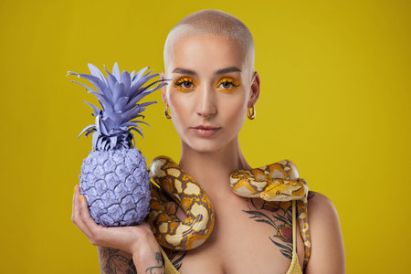 Keep them distracted. Shot shot of a woman holding a painted pineapple while posing with a snake...