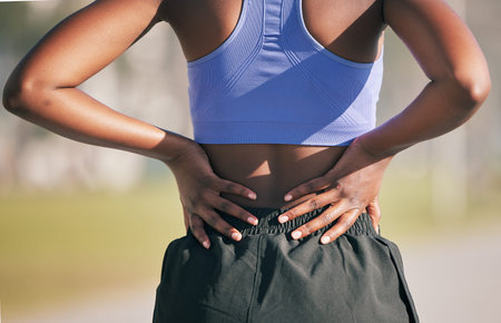 Runner woman, back pain and outdoor with hands, emergency and problem with spine, muscle and...