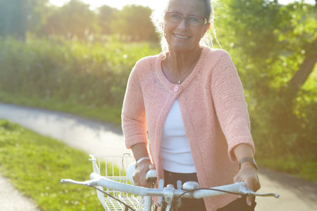 Portrait, smile and elderly woman on bike outdoor, exercise and fitness in summer. Happy, senior person on bicycle in nature or garden for cycling in countryside for body health, travel and glassesの写真素材