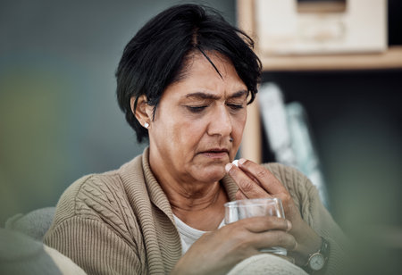 Depression, drinking water or old woman in home to take pills, vitamins or supplements as medicine. Medical, sick or lonely senior person taking drugs or medication tablets for fatigue or anxietyの写真素材