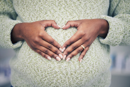 Pregnancy, closeup and woman with a heart shape on her maternal belly for care and motherhood. Health, zoom and African pregnant female person hands on stomach with a love sign or emoji for her baby.の写真素材