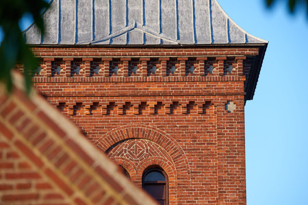 Closeup of a red face brick church steeple against a blue sky. Tall infrastructure and tower used to...