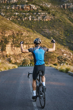 Man, cycling and celebration with back on mountain road, strong arm muscle or fist in air for winning. Winner athlete, bicycle or achievement for health, workout or training for performance in natureの写真素材