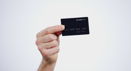 Hand, payment and closeup of credit card in a studio for online shopping, paying bills or debt. Ecommerce, money and zoom of person with bank account for buying products isolated by white background.の写真素材