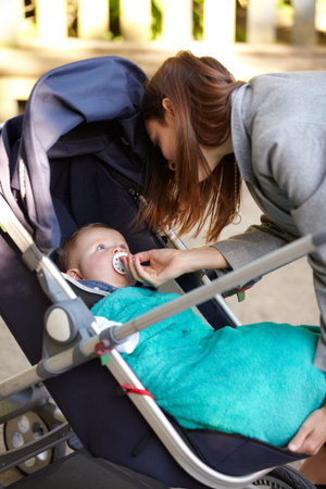 Mother, baby and pacifier in stroller for walk, together or bonding for exercise, health or wellness. Young woman, infant and giving of dummy for comfort, toddler or child with care in neighborhoodの写真素材