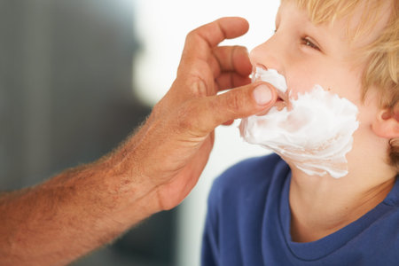 Showing him the ropes of shaving. A father playfully putting shaving cream on his sons face.