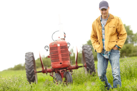 Nature walk. Full length image of a farmer standing next to his tractor in a field.の写真素材